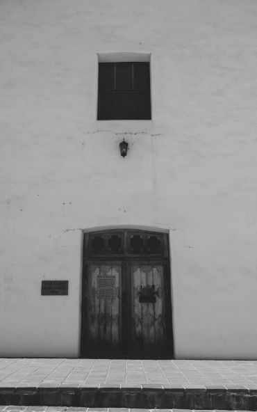 Old wooden door on a white stucco wall under a small window.