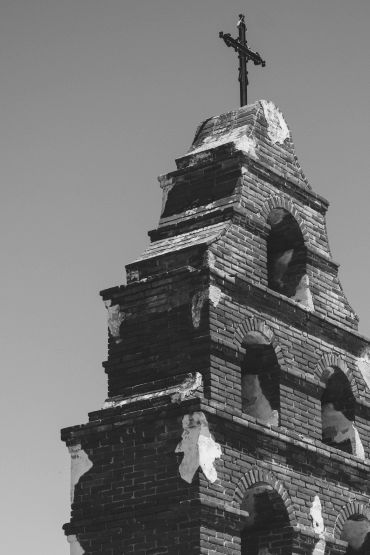 Old brick church tower with a cross on top under clear sky.