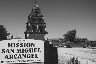 Historic Mission San Miguel Arcangel with bell tower and sign in black and white.