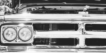 Close-up of a classic car's shiny chrome grille and headlights in black and white.