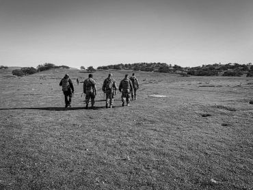 Five soldiers walking across an open field in black and white.