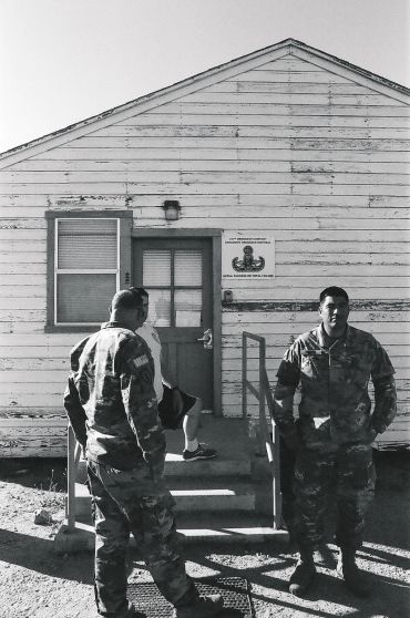 Two soldiers stand outside a weathered military building in black and white.