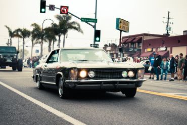 Classic car driving on a street with palm trees and spectators.