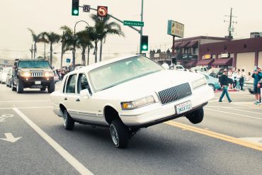 White limousine performing a hydraulic lift on one side on a street.