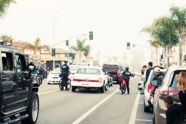 A busy street scene with cars, motorcycles, and people on the sidewalk.