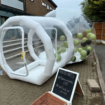 A large inflatable bubble with balloons inside and a sign with house rules outside.