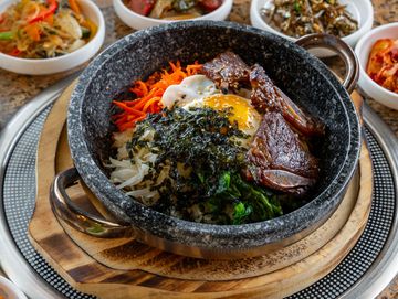 Korean bibimbap with various side dishes on a table.