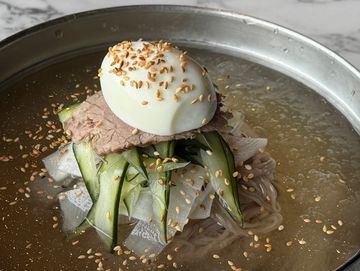 Cold noodle soup with sliced beef, cucumber, and a boiled egg topped with sesame seeds.