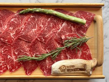 Thinly sliced marbled beef with asparagus, rosemary, and mushroom on a wooden board.