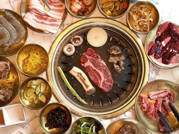 Korean BBQ with meat and various side dishes arranged around a grill.
