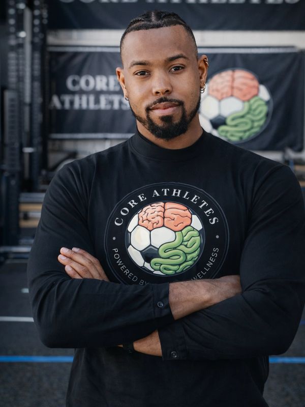 Man with crossed arms wearing a Core Athletes shirt featuring a brain and soccer ball logo.