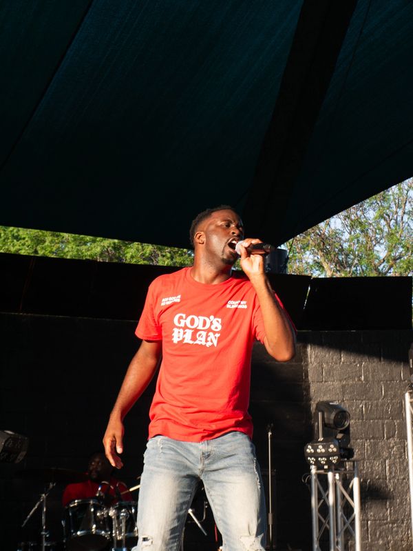 Man singing on stage wearing a red God’s Plan shirt.
