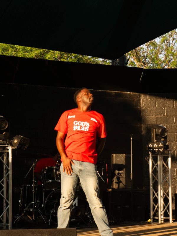 Man in red 'God's Plan' shirt performing on stage.