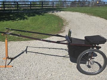 A lightweight horse-drawn cart with two wheels on a gravel path.