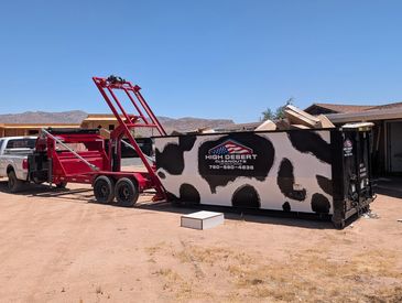 A truck with a red trailer and a large dumpster in a desert area.