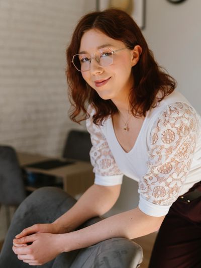 Young woman with glasses leaning on a chair, smiling gently.