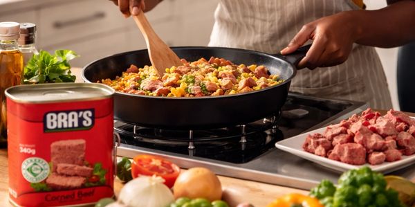 Woman cooking a colorful dish with corned beef in a bright kitchen.