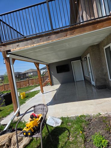 Backyard patio with swing and toys under a raised deck.