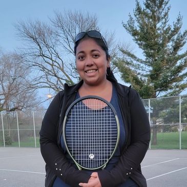 Smiling woman holding a tennis racket on an outdoor court during daylight.