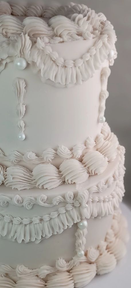 Elegant white tiered cake with intricate frosting and pearl decorations.