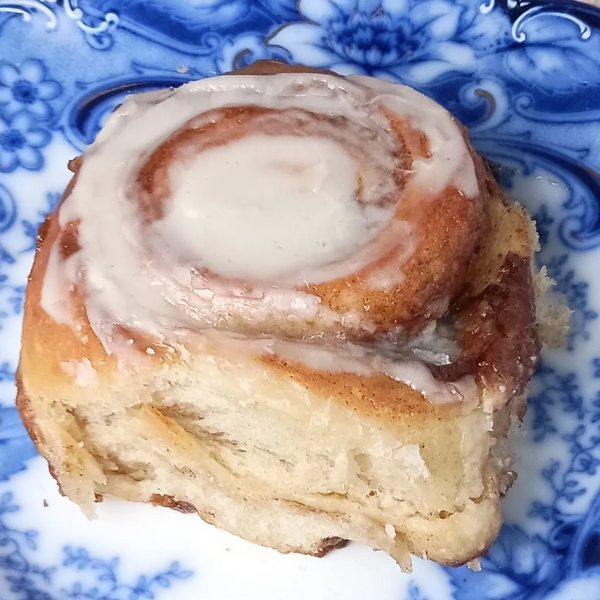 A frosted cinnamon roll on a blue and white floral plate.
