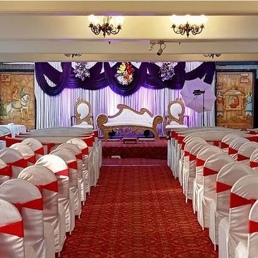 Elegant wedding stage with white and red chair covers and ornate backdrop.