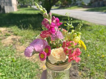 Hand holding a jar with a colorful bouquet of wildflowers outdoors.