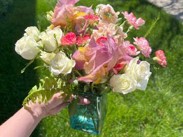 Hand holding a vibrant bouquet of mixed flowers in a blue vase.