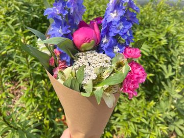 A vibrant hand-held bouquet with purple, pink, and white flowers wrapped in brown paper.
