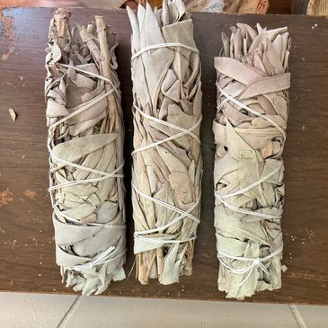 Three bundles of dried sage leaves tied with string on a wooden surface.