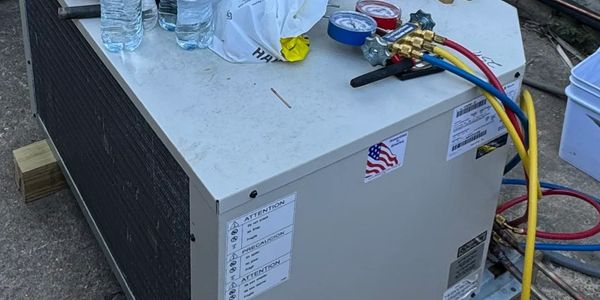Portable HVAC unit with gauges and hoses connected, placed outdoors.