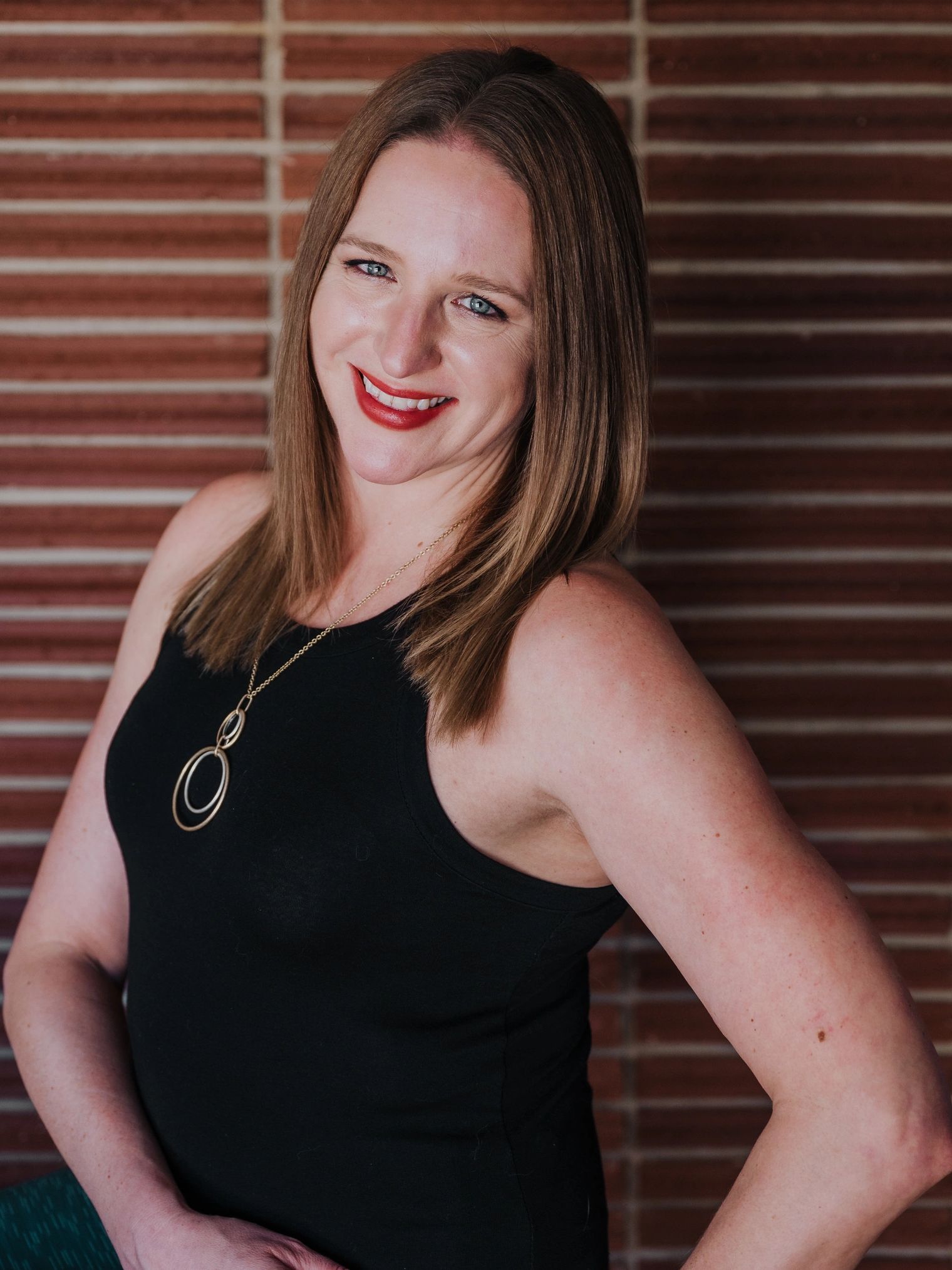 Beth Steffens smiling into the camera with her hands on her hips, in front of a brick wall.