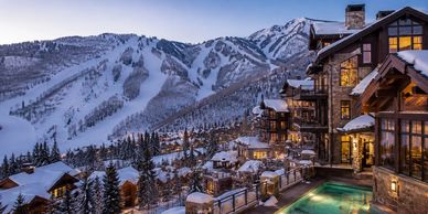 Luxury mountain lodge with snowy peaks and outdoor pool at dusk.