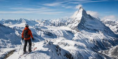 Hiker overlooking snowy mountain peaks with a clear sky.
