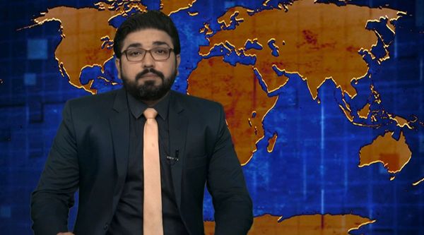 News anchor in black suit with a peach tie in front of a world map.