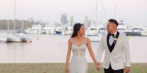 Bride and groom holding hands by the marina with boats in the background.