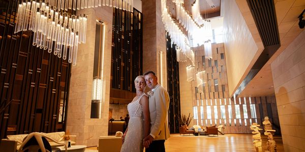 Couple in wedding attire posing in a luxurious, modern lobby with dramatic lighting.