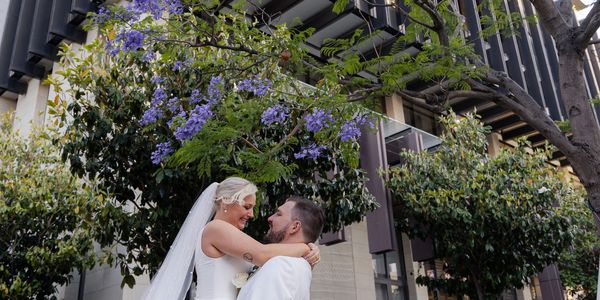 Bride and groom sharing a joyful moment under purple blossoms.