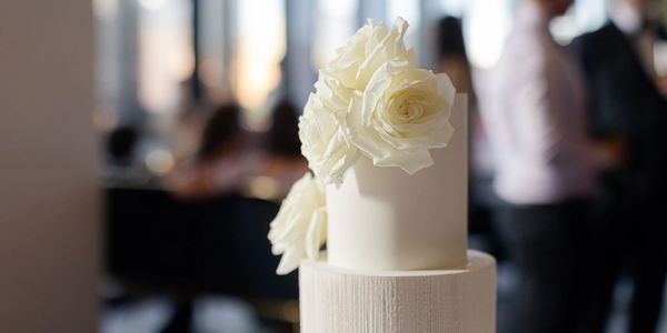 Elegant white cake decorated with white roses at a formal event.