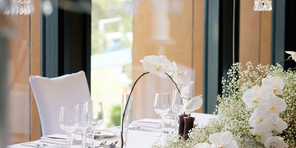 Elegant dining table set with white flowers and glassware by a window.