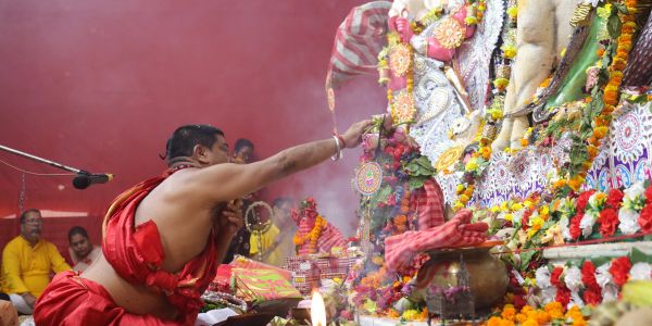 A priest performing a Hindu ritual with flowers and incense.