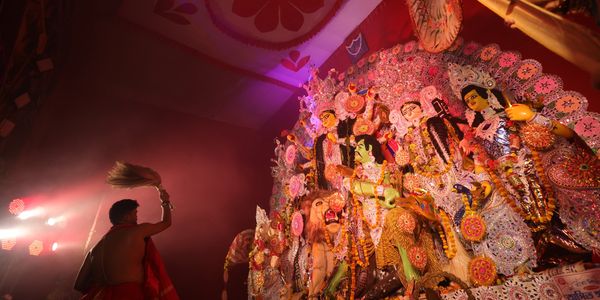 A person performing a ritual in front of colorful Hindu deity idols.