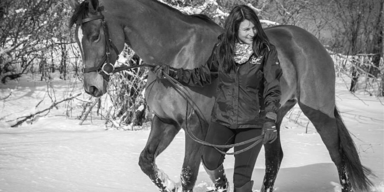 A woman leads a horse through snowy terrain, both enjoying the winter day.
