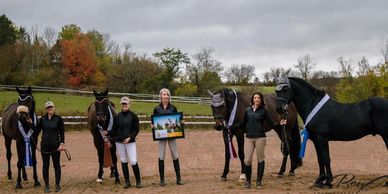 Four women standing with their horses, displaying awards and a framed picture outdoors.