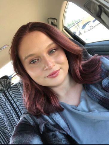 Young woman with red hair sitting in a car, smiling.