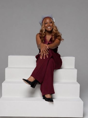 Woman in maroon outfit smiling while sitting on white steps.