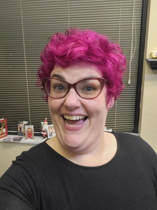 Person with bright pink curly hair smiling joyfully.