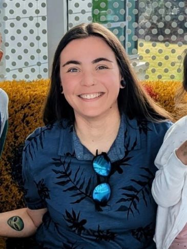 Smiling woman with long dark hair and sunglasses on shirt.