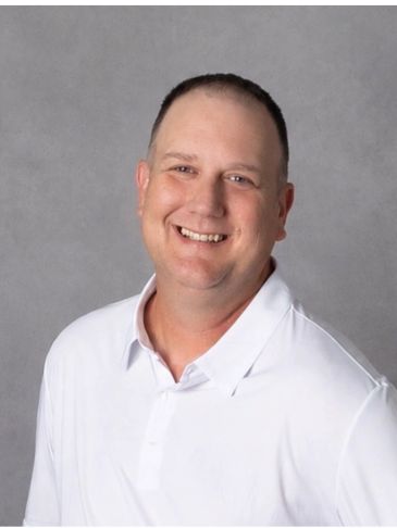Smiling man in white polo shirt against gray background.