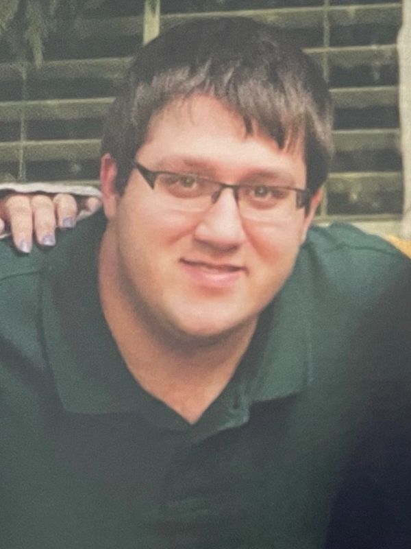 A man wearing glasses and a dark green shirt smiling at the camera.